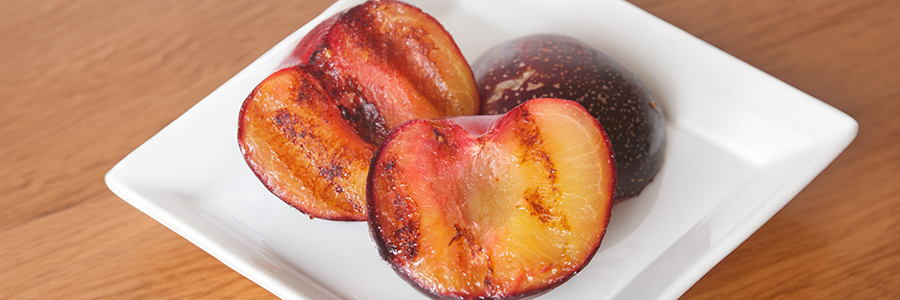 Close up of two grilled plum halves on a white plate.