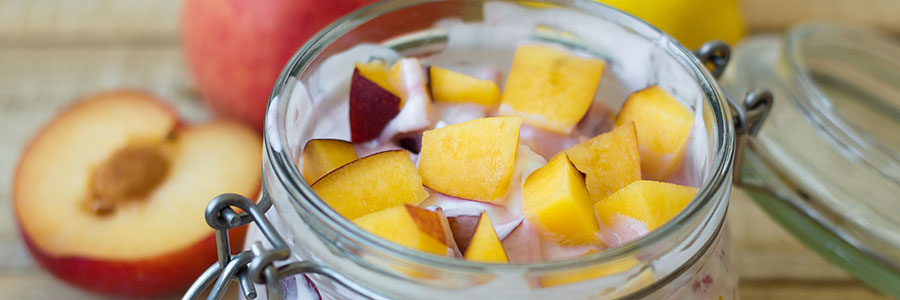 Close shot of a jar filled with creamy fruit salad with yogurt, peaches, and plums.