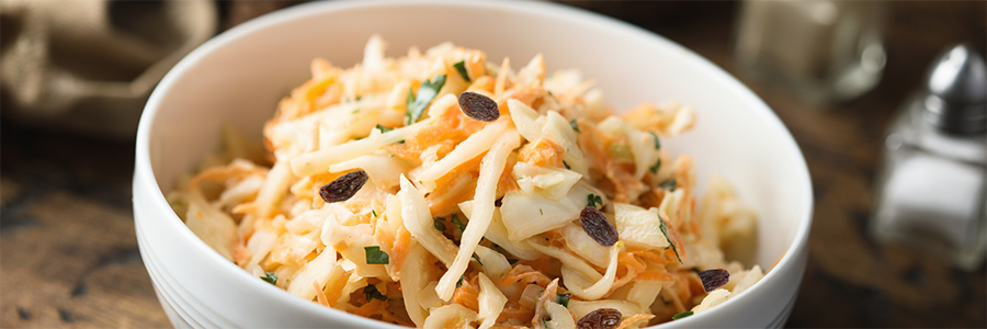 Shot of a bowl of slaw with shredded cabbage, carrots, apples, and raisins.