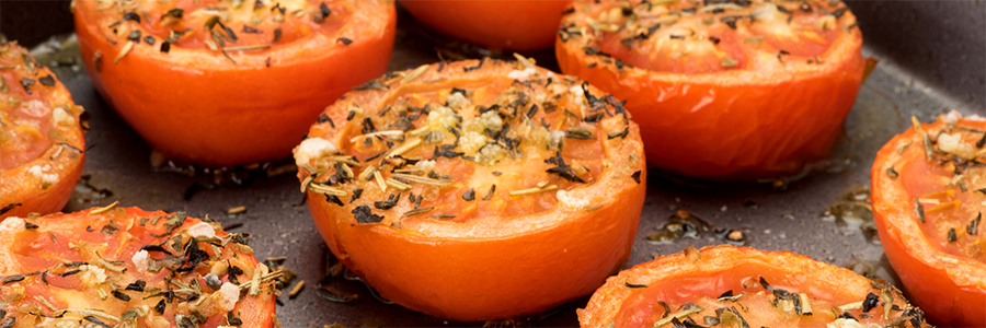 Close up of halved tomatoes roasted and topped with herbs and Parmesan cheese.