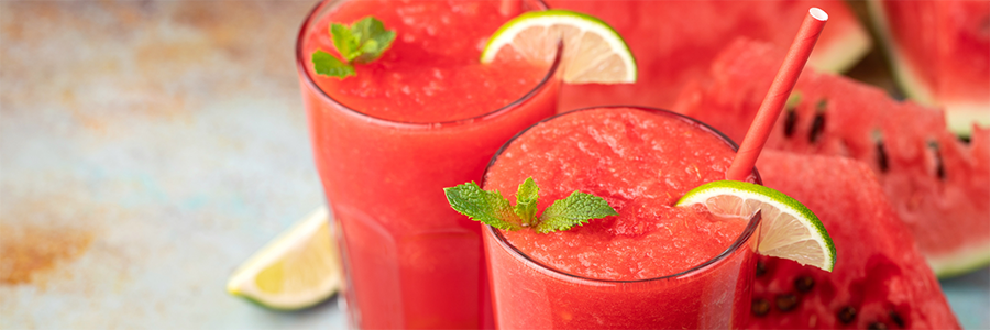 Shot of two tall glasses with watermelon slushies. Garnished with lime slices and mint.