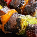 Close up shot of kabobs with beef, yellow pepper, yellow squash, and onions.