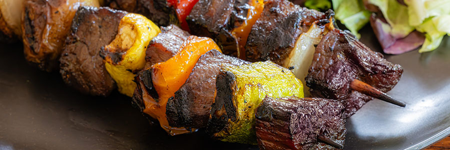 Close up shot of kabobs with beef, yellow pepper, yellow squash, and onions.