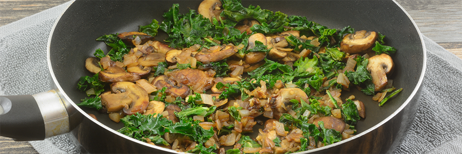 Shot of pan with sautéed greens and mushrooms.