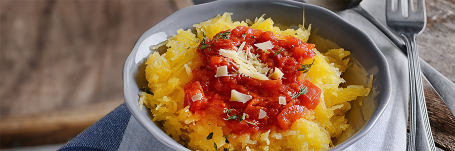 Shot of a bowl of roasted spaghetti squash topped with a chunky tomato sauce and garnished with shaved Parmesan cheese.