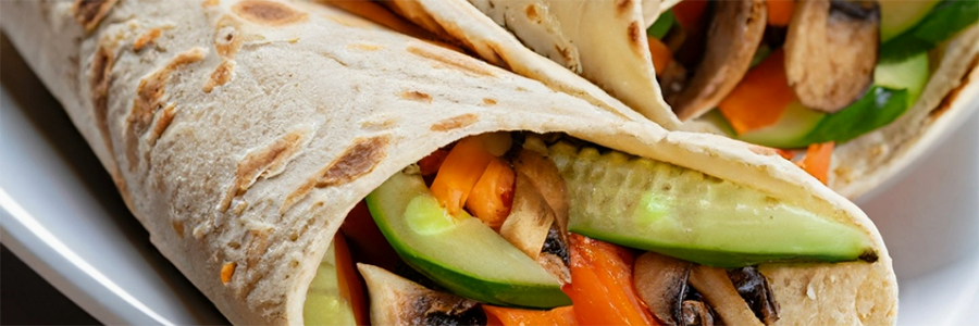 Shot of whole wheat tortilla wrapped around sliced vegetables, including cucumbers, carrots, and mushrooms.
