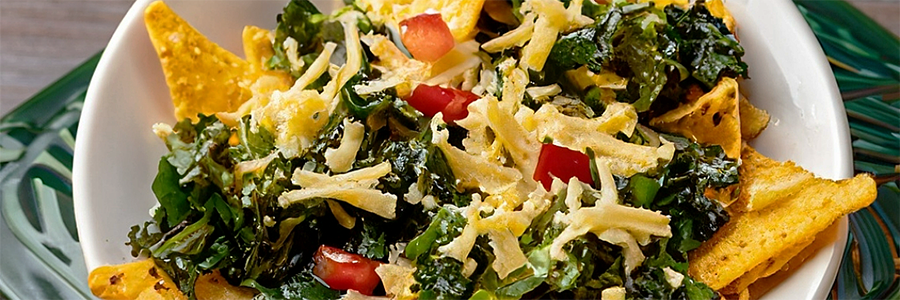 Close up shot of a plate of veggie nachos topped with sautéed kale, red peppers, and shredded cheese.