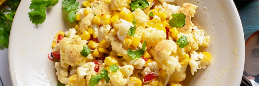 Close up shot of a plate of veggies, including cauliflower, corn, peppers, onions, and garnished with cilantro.