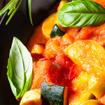Close up shot of a pan with sliced zucchini in marinara sauce. Pan is garnished with basil leaves.