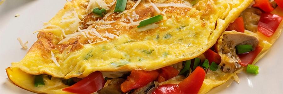 Close up shot of an omelet with red peppers and artichoke hearts. Garnished with sliced green onions.