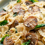 Wide shot of a stoneware dish with bow-tie pasta, spinach, and mushrooms.