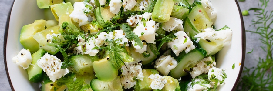 Close up of a mixed salad with cucumbers, avocado, shallots, dill, and crumbled feta cheese. Salad is garnished with dill.