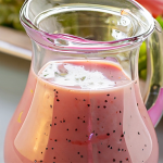 Wide shot of a carafe of pink poppyseed dressing with a large salad in the background.