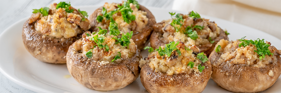 Wide shot of a plate of baked mushrooms stuffed with a mixture of breadcrumbs, peppers, and herbs. Garnished with parsley.