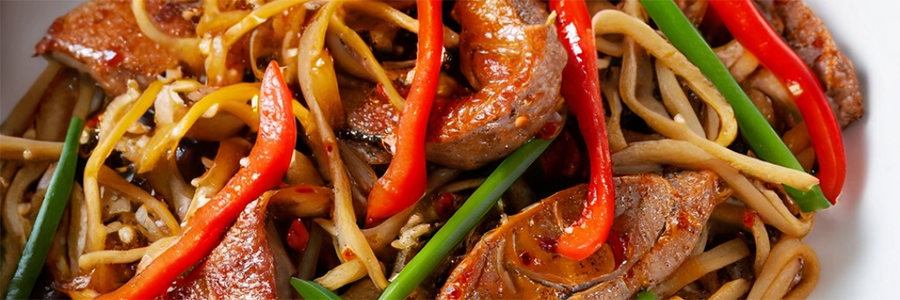 Close up shot of a stir fry with strips of pork tenderloin, red bell pepper, and green onion with noodles in a chili-garlic sauce.