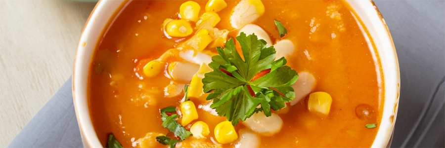 Close up shot of a bowl of soup with pureed squash, corn, and hominy. Garnished with parsley.