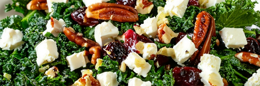 Close up shot of a salad with kale, pecans, apples, feta cheese, and dried cherries.
