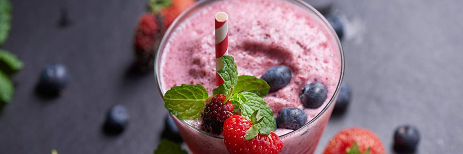 Wide shot of a pink-colored smoothie garnished with blueberries, strawberries, and a red and white striped straw.