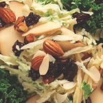 Close up shot of a slaw with shredded rutabaga, apples, pears, and kale. Slaw is garnished with dates and almonds.