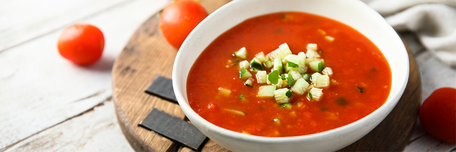 Shot of a while bowl filled with gazpacho. The soup is garnished with diced cucumber.