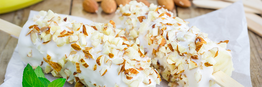 Close up of two bananas dipped in yogurt and topped with chopped nuts.