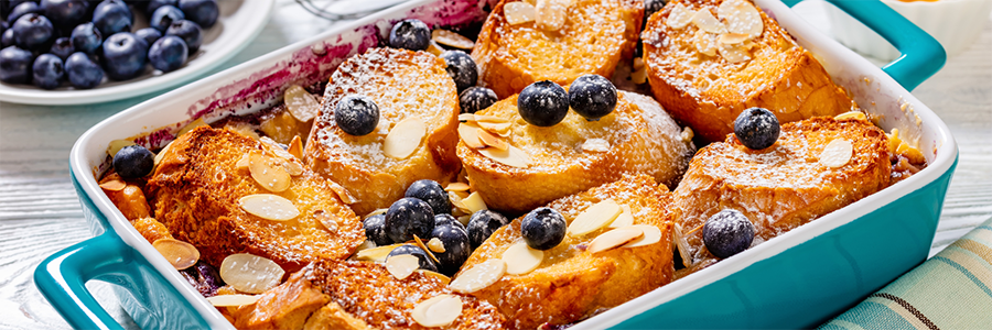 A blue casserole dish with slices of French toast topped with blueberries and confectioner's sugar.