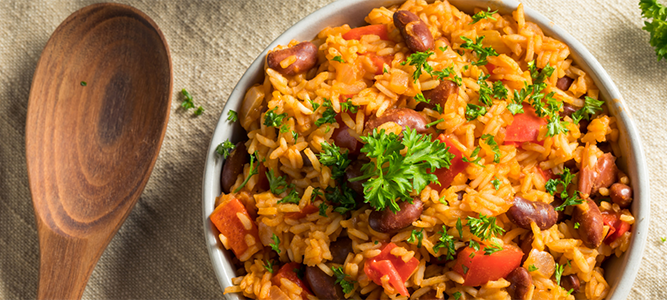 Wide shot of a bowl of seasoned rice with beans and tomatoes. Rice is garnished with sprigs of fresh parsley.