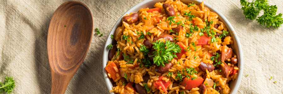 Wide shot of a bowl of seasoned rice with beans and tomatoes. Rice is garnished with sprigs of fresh parsley.