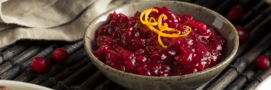 Shot of a stoneware bowl containing cranberry sauce with bits of fresh cranberries. Sauce is garnished with orange zest.