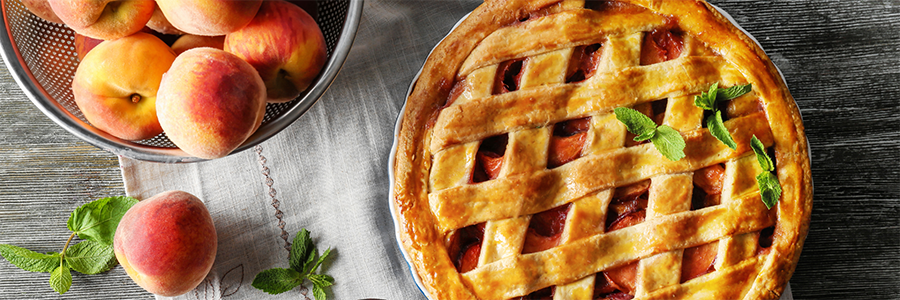 Wide shot of a peach cobbler with a latticed crust. A bowl of peaches is placed beside the pie for decoration.