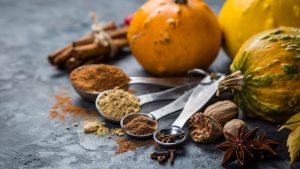 Shot of four measuring spoons with various spices. Displayed with seasonal gourds in the background.