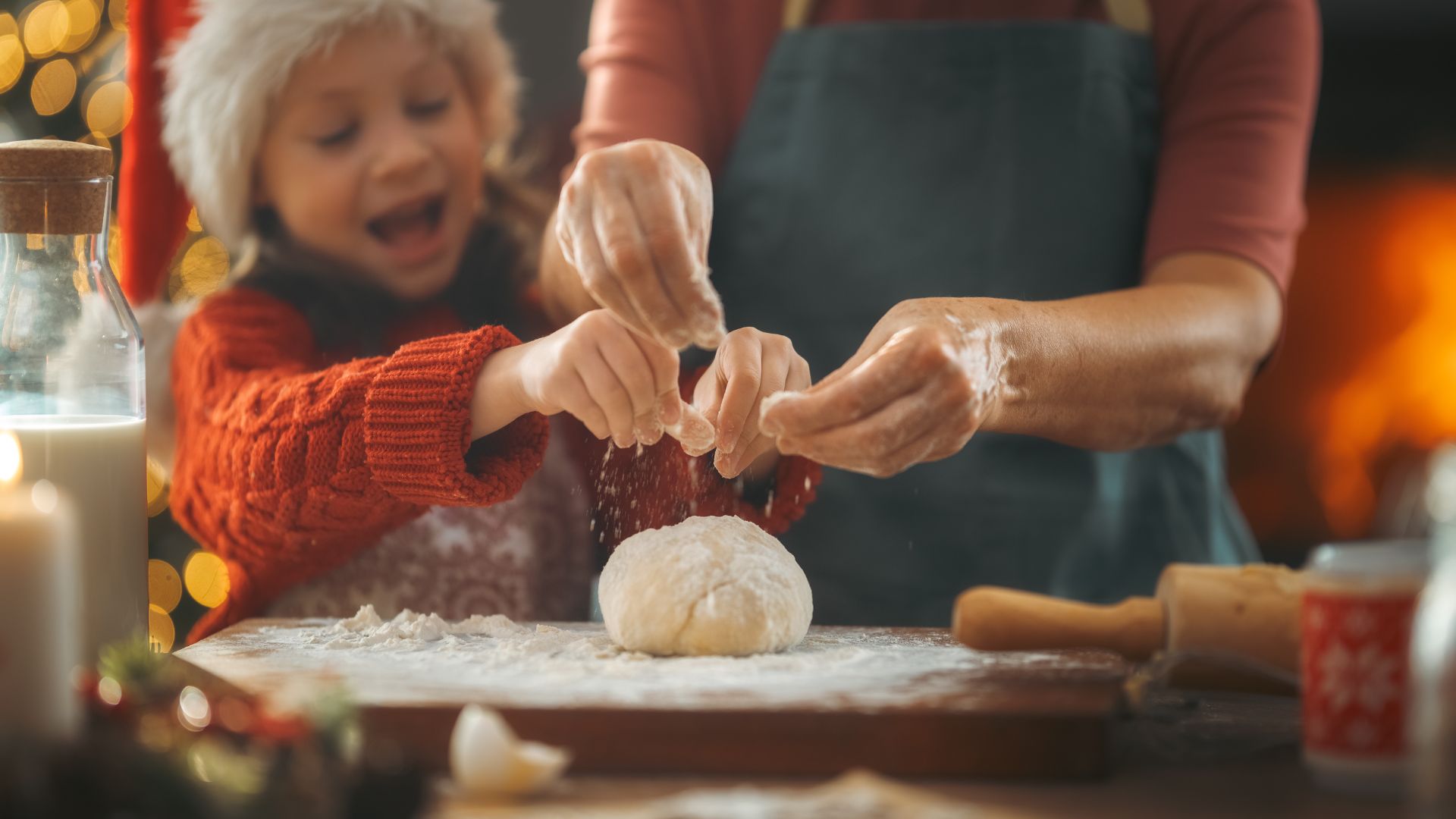 A young girl and her mother sprinkling flyer on dough. The young girl is wearing a red Santa hat with faux-fur trim.