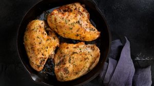 Shot of three herb seasoned chicken breasts baked in a cast-iron skillet.