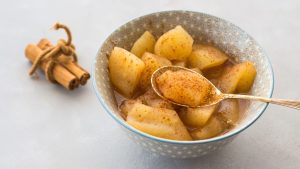 Close up of cooked apple chunks with cinnamon with a gold spoon in a gray stone bowl.