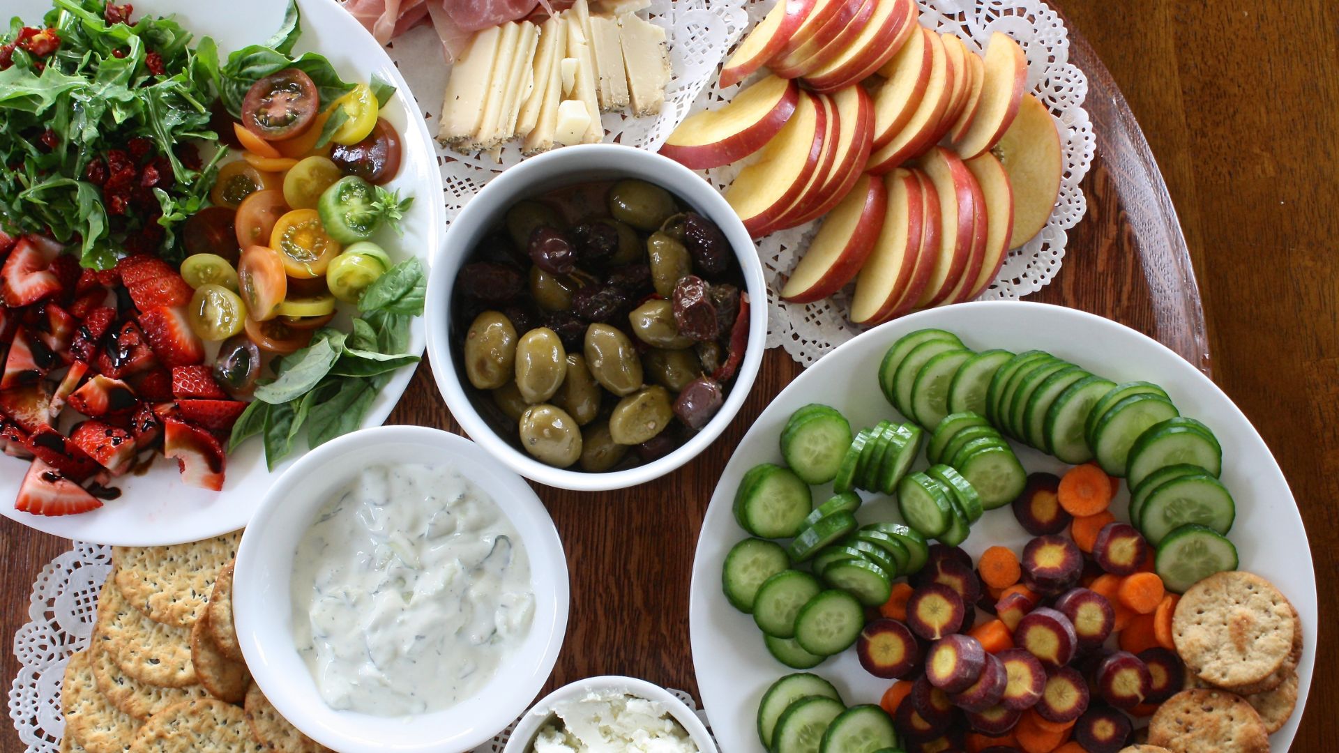 A table displaying an assortment of fresh vegetables, fruit, crackers and dips.