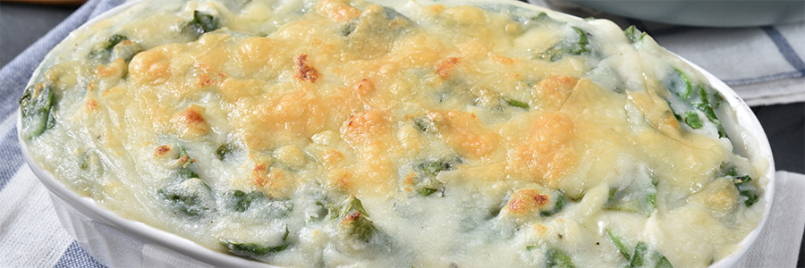 Close up of a casserole dish with a mixture of baked mashed potatoes and spinach, topped with melted mozzarella cheese.