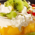 Shot of a dessert dish with fruit cocktail, pineapple, and kiwi. Topped with whipped topping.