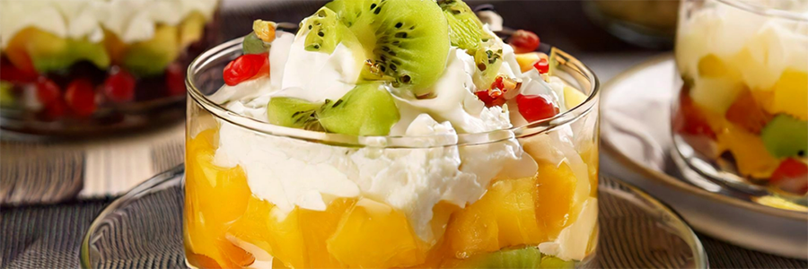 Shot of a dessert dish with fruit cocktail, pineapple, and kiwi. Topped with whipped topping.