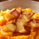 Shot of a shallow bowl with mashed butternut squash topped with diced apples and sprinkled with cinnamon.
