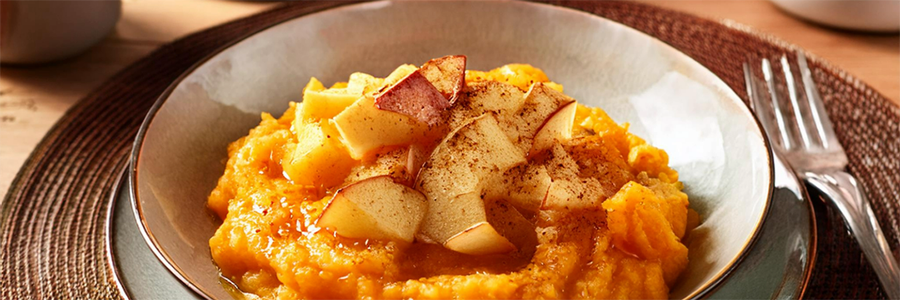 Shot of a shallow bowl with mashed butternut squash topped with diced apples and sprinkled with cinnamon.