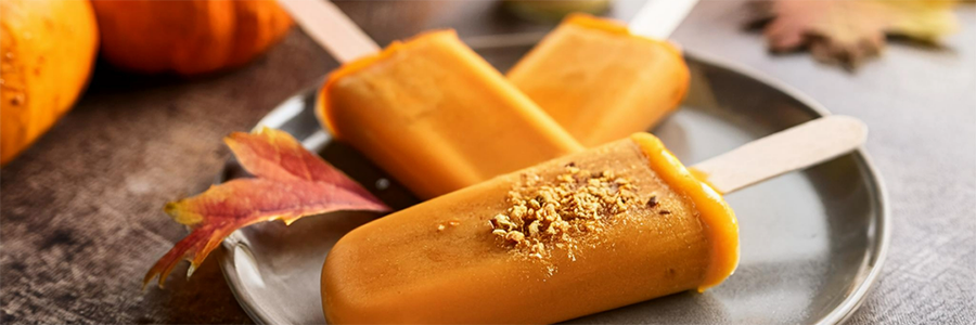 Wide shot of three pumpkin popsicles on a plate.