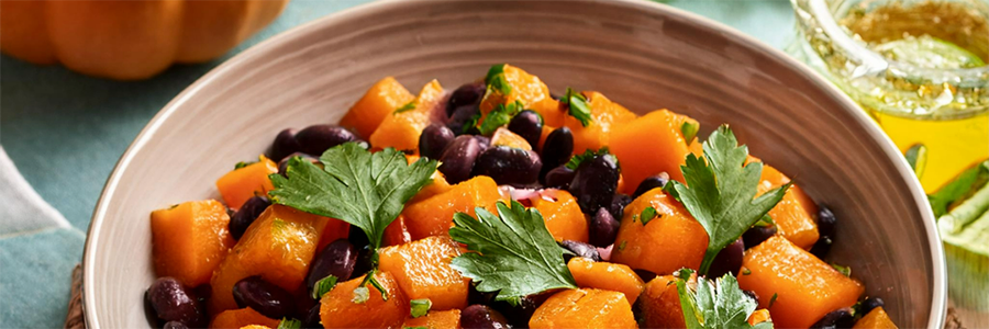 Shot of a bowl with sautéed squash and black beans, garnished with sprigs of parsley.