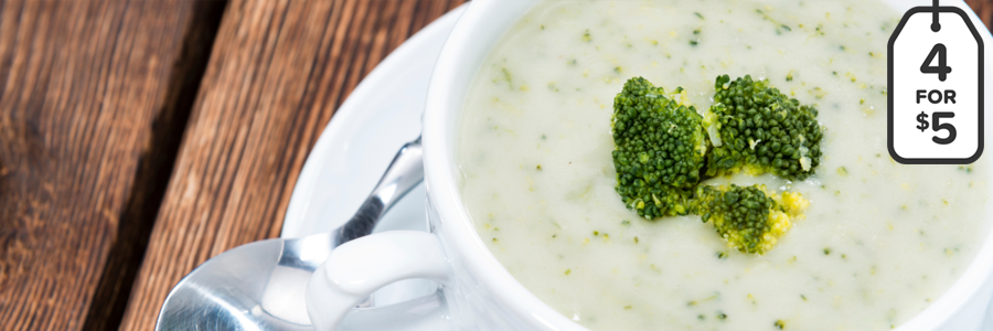 Close up shot of a white mug filled with broccoli soup. Mug is garnished with 3 small broccoli florets.