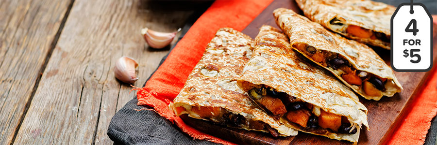 Close up of quartered quesadillas on a wooden platter. Quesadillas are filled with sweet potatoes and black beans.