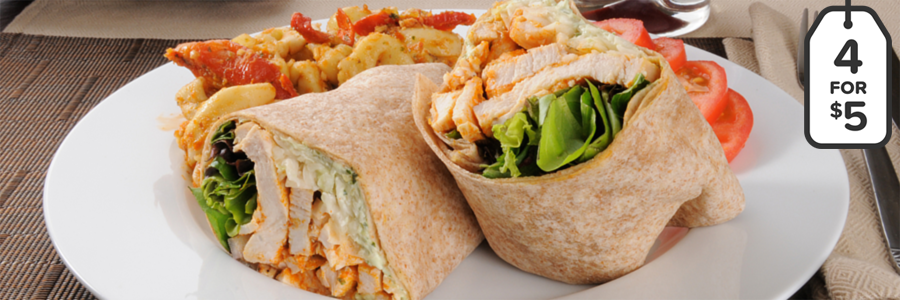 Wide shot of a sandwich wrap with chicken and veggies wrapped in a whole wheat tortilla. Sandwich wrap is cut into two and displayed on a white plate with tomato slices on the side as garnish.