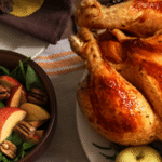 Wide shot of a dining table with a whole roasted turkey in the center. Turkey is flanked by a bowl of mashed potatoes, tossed salad, and pumpkin pie.