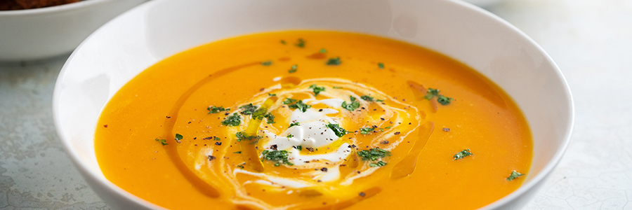 Close up of bowl of carrot orange soup, garnished with fresh herbs.