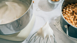 Overhead shot of a mixing bowl and mixing whisk with merengue made from aquafaba displayed next to a bowl of chickpeas.