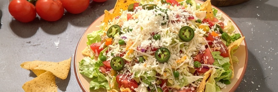A plate of salad with lettuce, tomatoes, and green peas. Garnished with cotija cheese and sliced jalapenos.