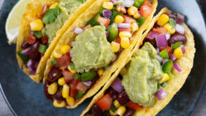 Close up image of tacos filled with black beans, corn, onions, and Pico de Gallo. Topped with a dollop of guacamole.